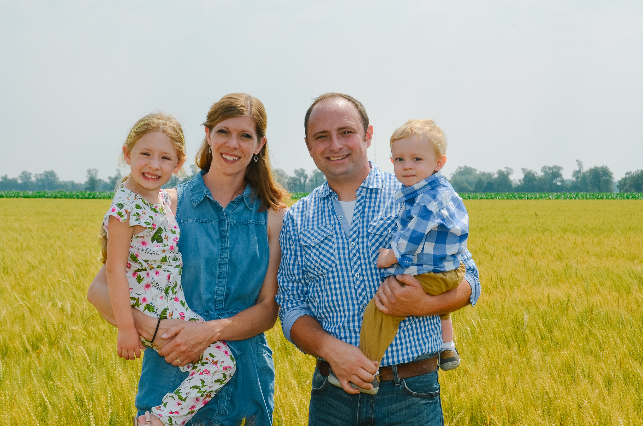 A family standing in a wheat field smiling at the camera.
