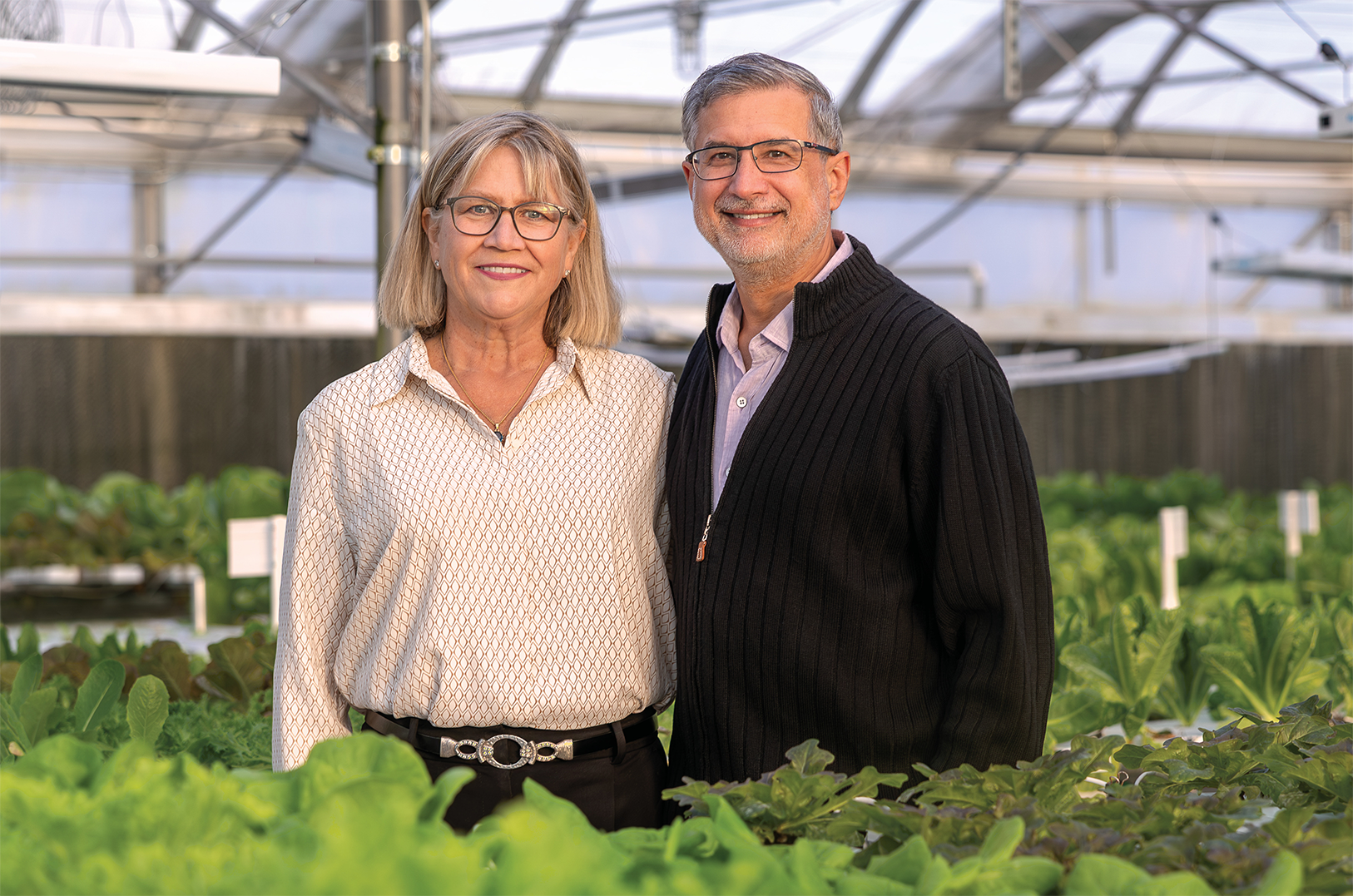 A smiling couple stands in a greenhouse.