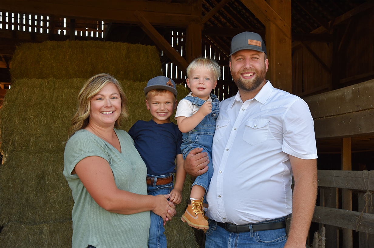 Family smiling at the camera in front of hay and a barn.