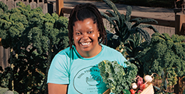 A woman holding vegetables in her garden.
